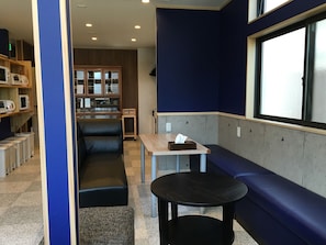 A seating area with a bench and a table, a kitchenette in the background, and a window with a view. - Guesthouse Orange Cabin (Fujikawaguchiko)