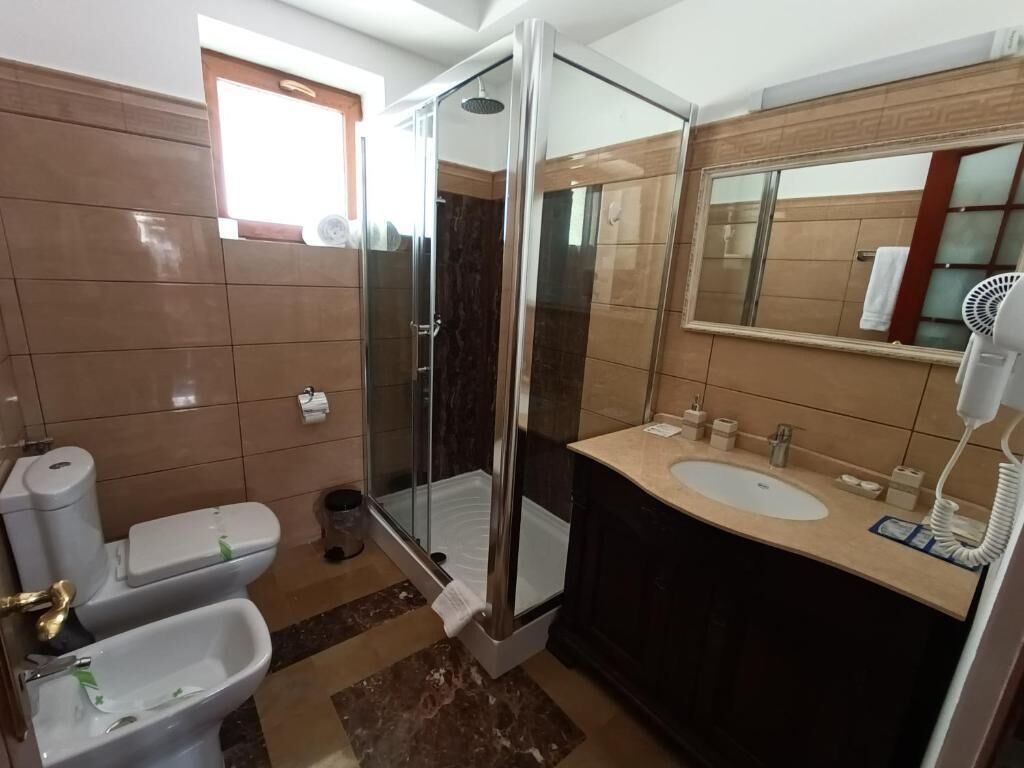 A bathroom with a glass-enclosed shower, a sink, a toilet, and a mirror.