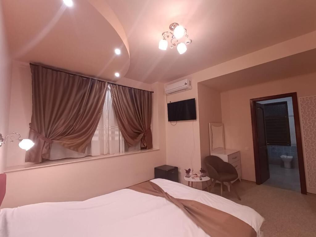 A hotel room with a bed, a desk, a chair, a TV, and a bathroom visible through an open door.