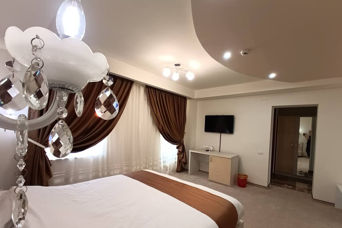 Habitación de hotel moderna con cama, escritorio, televisión y baño visible a través de una puerta abierta.