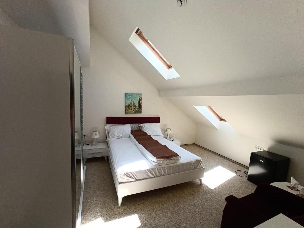 A bedroom with a bed, bedside tables, a desk, and a chair. There are skylights on the ceiling.