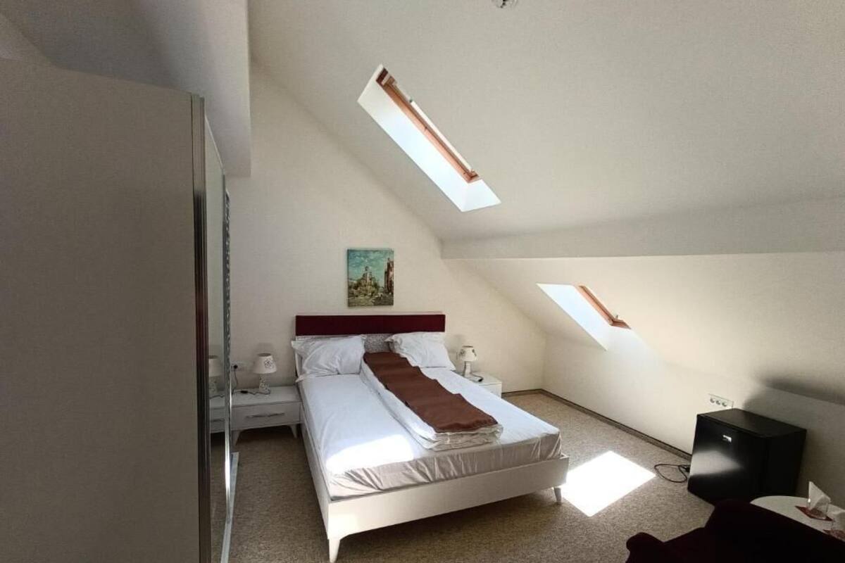 Un dormitorio con cama, mesitas de noche, un escritorio y una silla. Hay tragaluces en el techo.