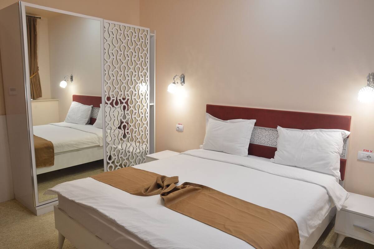 Habitación de hotel con cama, mesita de noche, espejo y un separador decorativo.