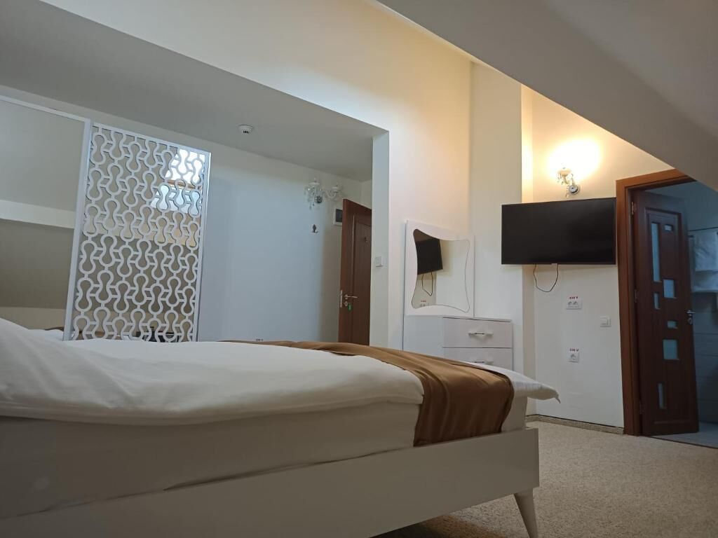 A bedroom with a bed, a TV mounted on the wall, a door, and a white wall.