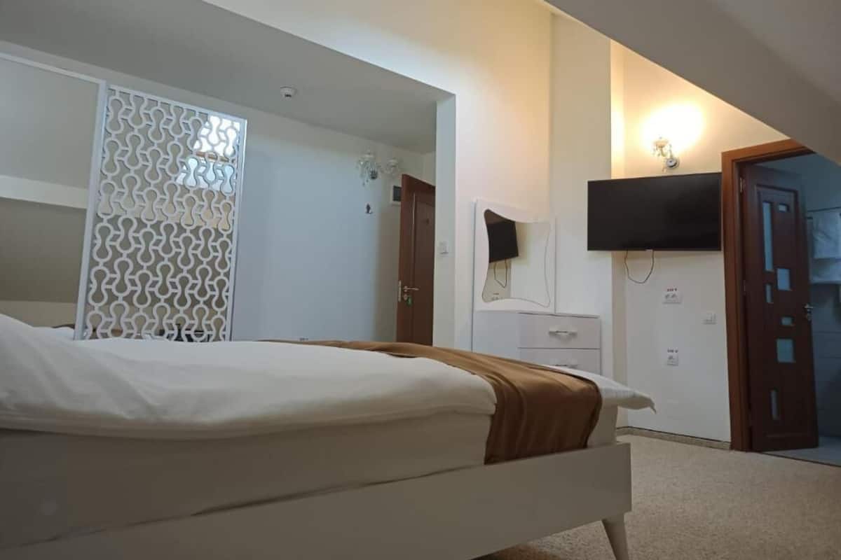 Un dormitorio con una cama, un televisor montado en la pared, una puerta y una pared blanca.