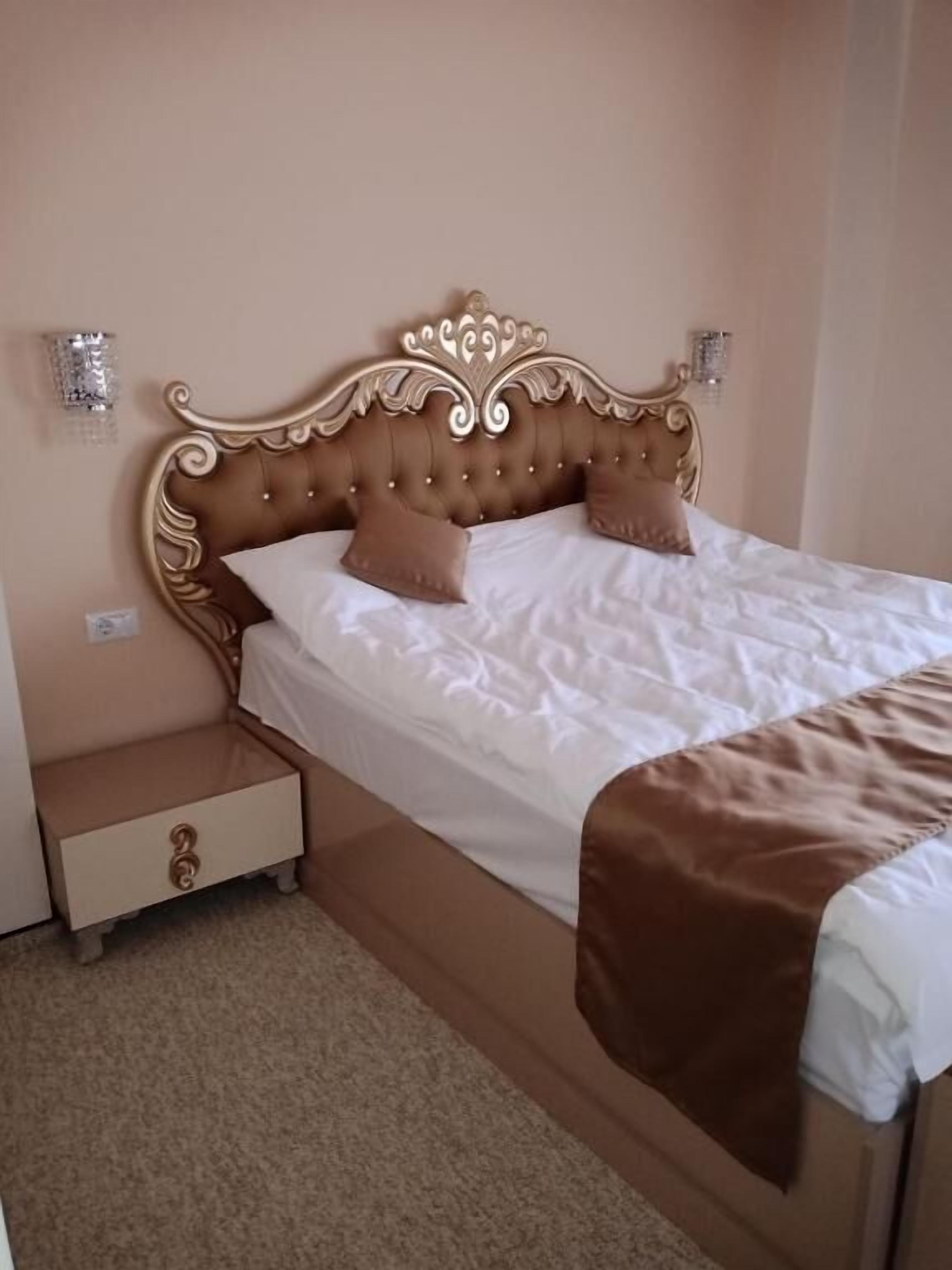 A bedroom with a tufted headboard, two bedside tables, a bed with white bedding, and a brown throw blanket.