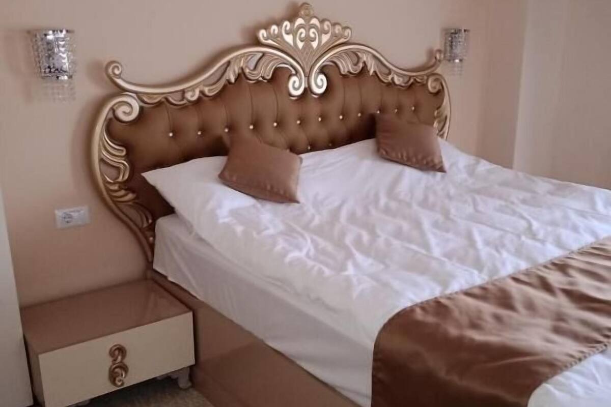 Un dormitorio con un cabecero capitonado, dos mesitas de noche, una cama con ropa de cama blanca y una manta marrón.