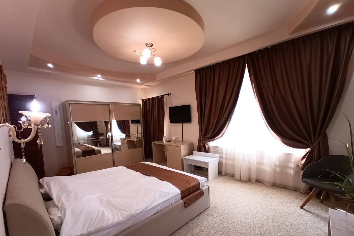 Una habitación de hotel con una cama grande, un escritorio, una silla, un televisor y una lámpara en el techo.
