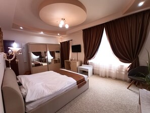 A hotel room with a large bed, a desk, a chair, a TV, and a ceiling light. - Virginia Gardens  (Baile Govora)