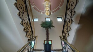 A grand staircase with ornate railings, a central chandelier, and a potted palm tree. - Virginia Gardens  (Baile Govora)