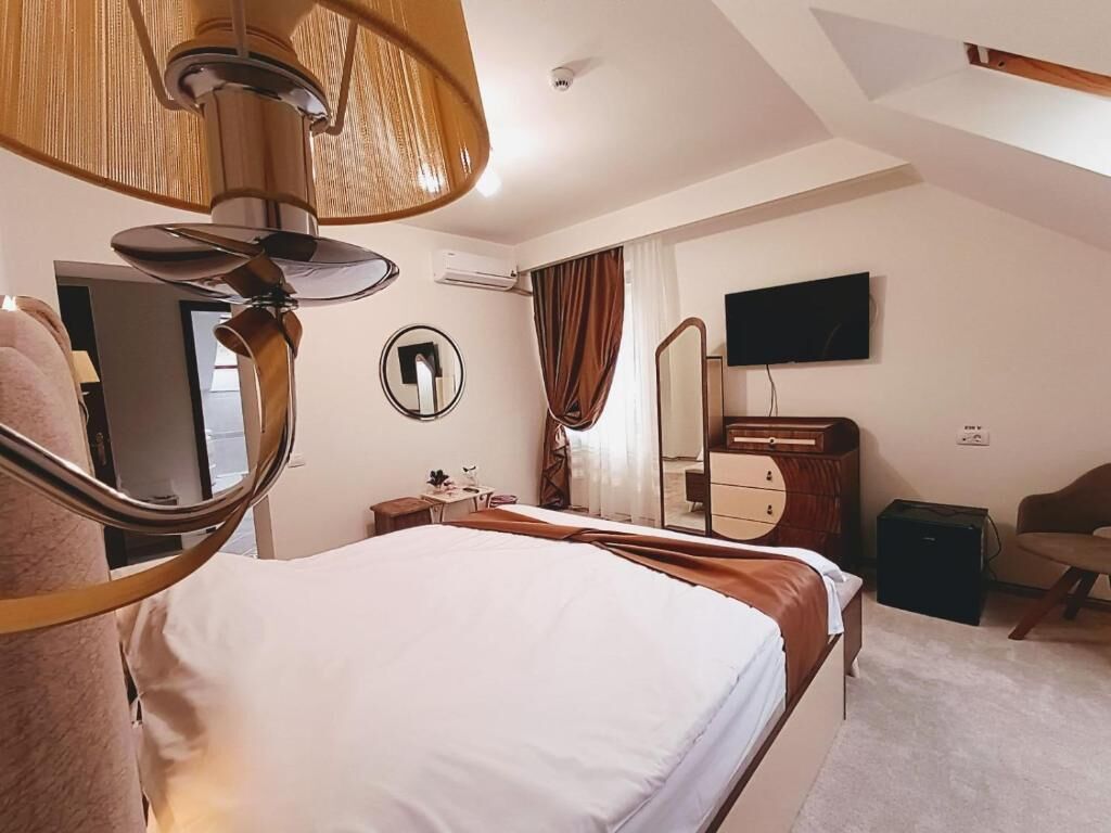 A hotel room with a bed, a desk, a chair, a television, a mirror, and a ceiling fan.