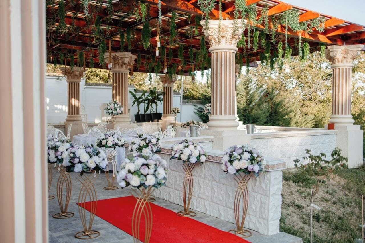 An outdoor wedding venue with columns, floral arrangements, and a red carpet.