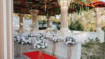 An outdoor wedding venue with columns, floral arrangements, and a red carpet.