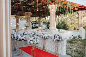 An outdoor wedding venue with columns, floral arrangements, and a red carpet.