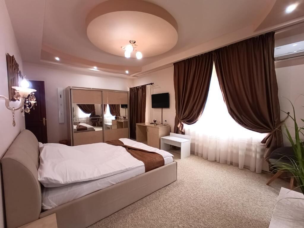 A hotel room with a bed, a desk, a mirror, a TV, and a large window with curtains.