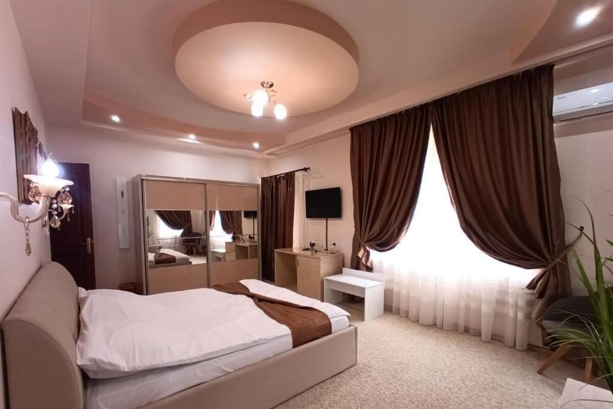 Habitación de hotel con cama, escritorio, espejo, televisor y un amplio ventanal con cortinas.