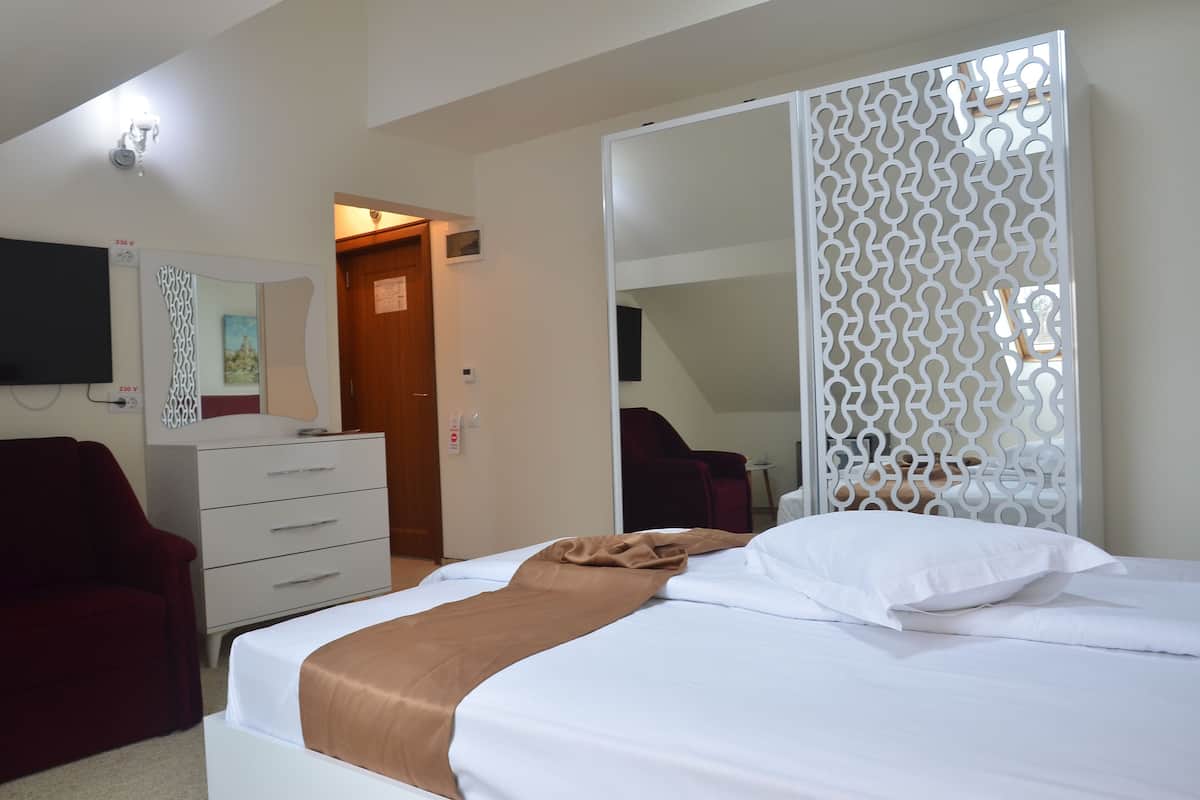 Habitación de hotel con una cama, una silla roja, un tocador blanco, un televisor y un panel decorativo blanco.