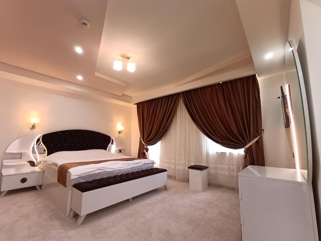 A modern hotel room with a bed, bedside tables, a nightstand, a bench, a dresser, and a mirror.