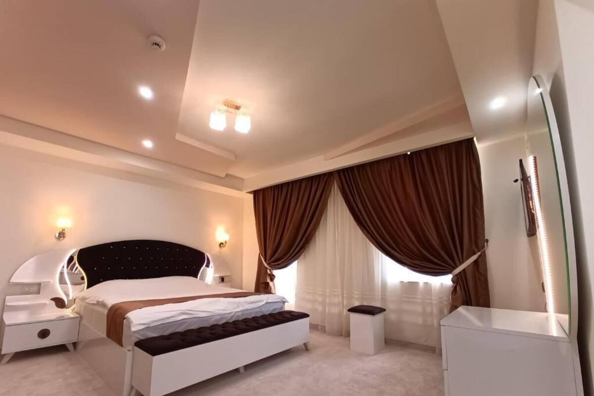 Una habitación de hotel moderna con cama, mesitas de noche, un banco, cómoda y espejo.