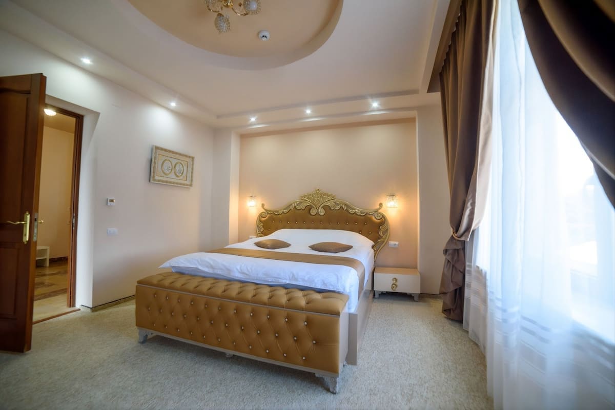 Un dormitorio con una cama grande, una mesita de noche, una lámpara de pared y una puerta que da a otra habitación.