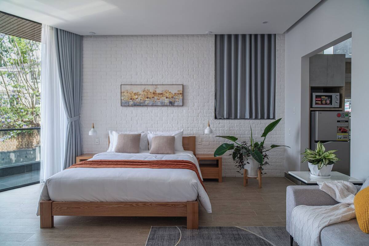 Un dormitorio moderno con una cama de madera, una pared de ladrillo blanco y vistas a la vegetación exterior.