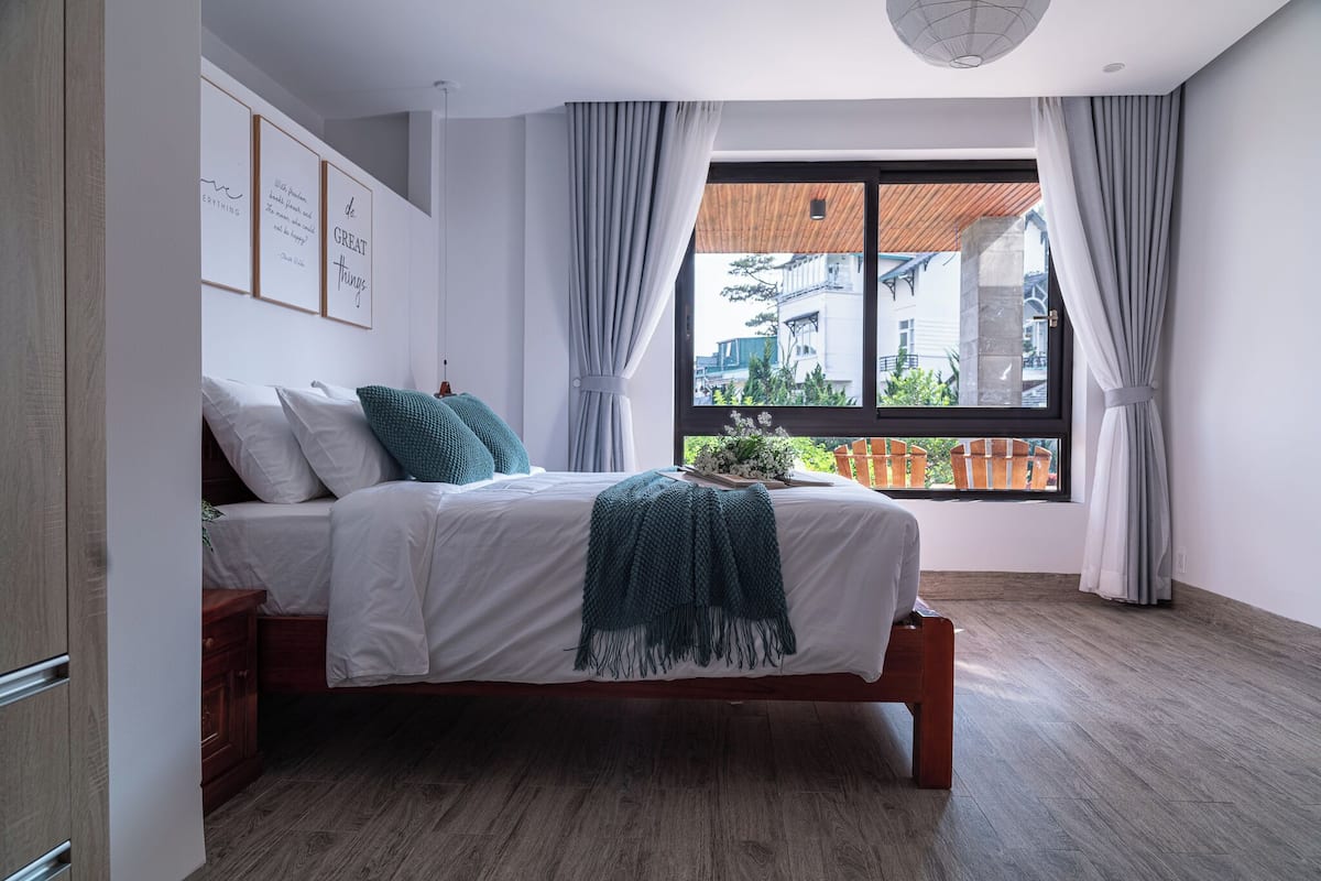 Un dormitorio con cama, ventana con cortinas, vistas a edificios y citas enmarcadas en la pared.