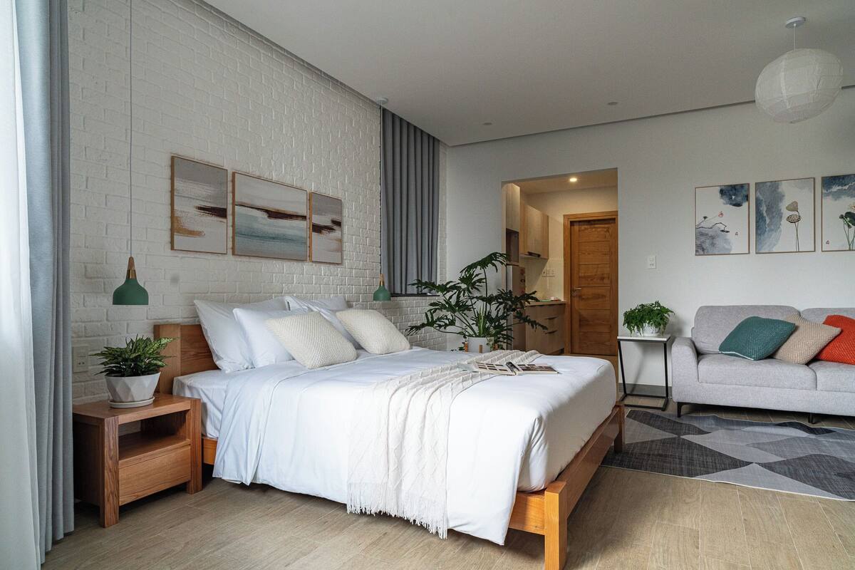 Un dormitorio moderno con cama, mesitas de noche, sofá y obras de arte en las paredes.