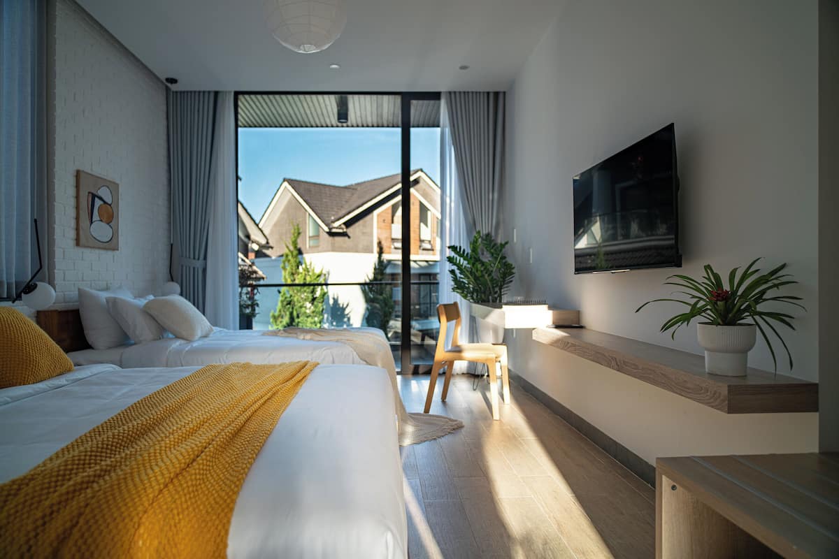 Habitación de hotel moderna con dos camas, un balcón, un televisor y una planta en maceta.