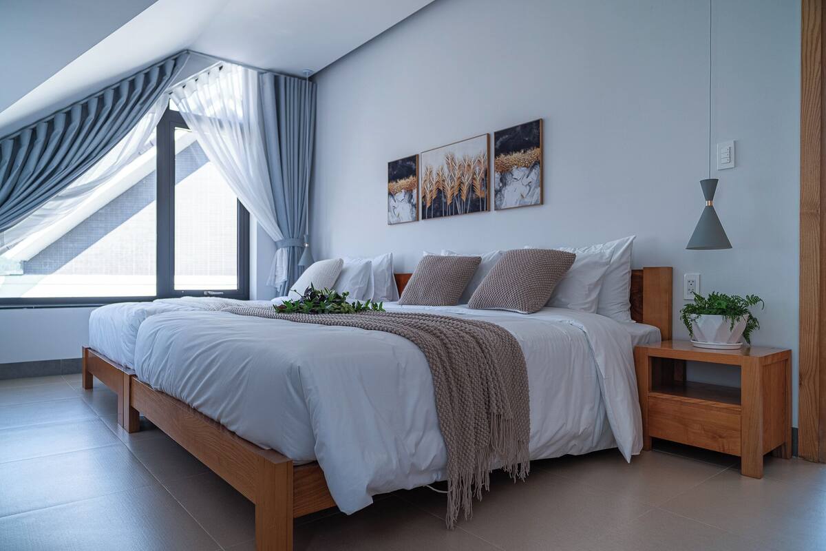 Un dormitorio moderno con una cama de madera, una mesita de noche con una planta y un ventanal con cortinas.