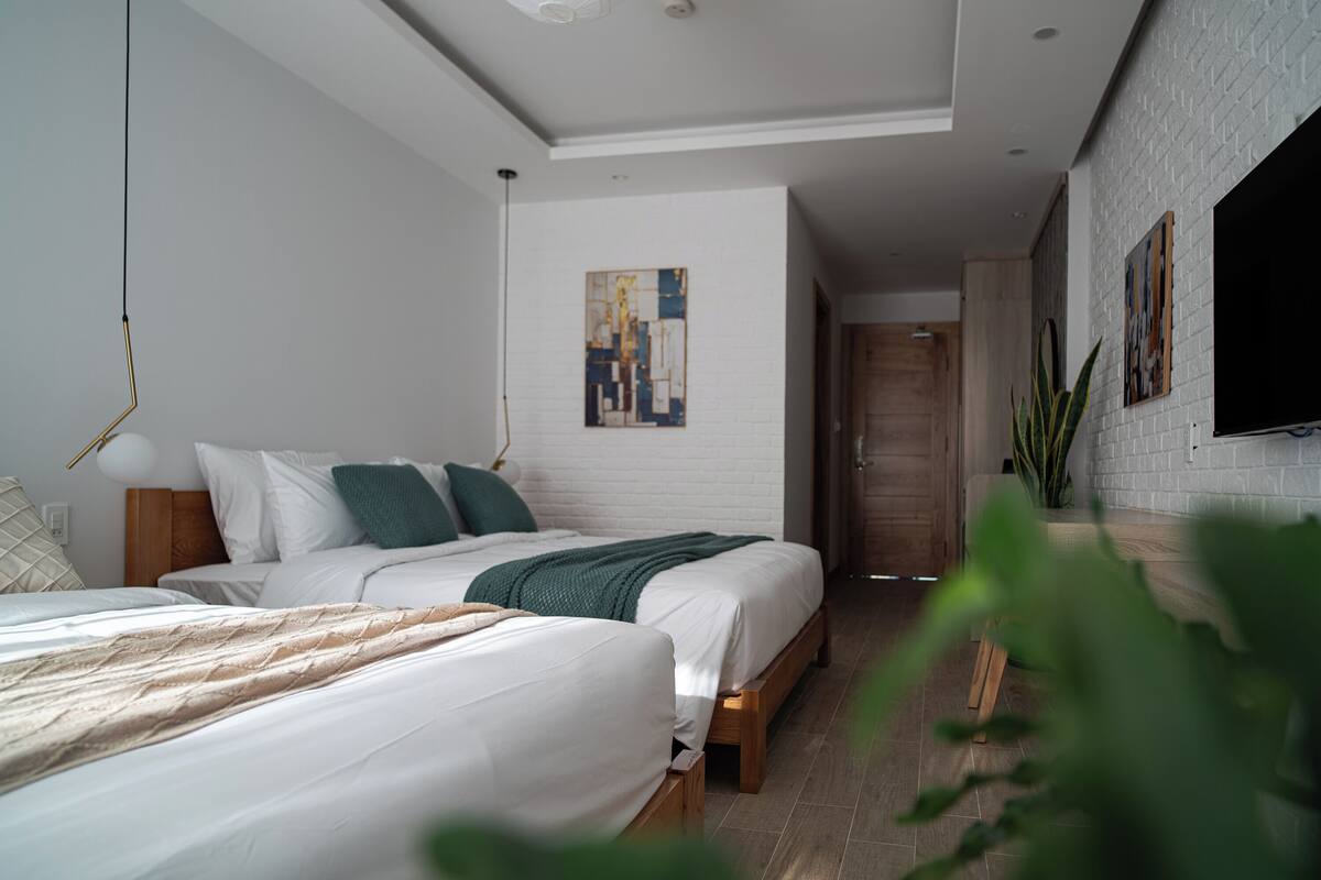 Un dormitorio moderno con dos camas, una pared de ladrillo blanco, un cuadro y un televisor.