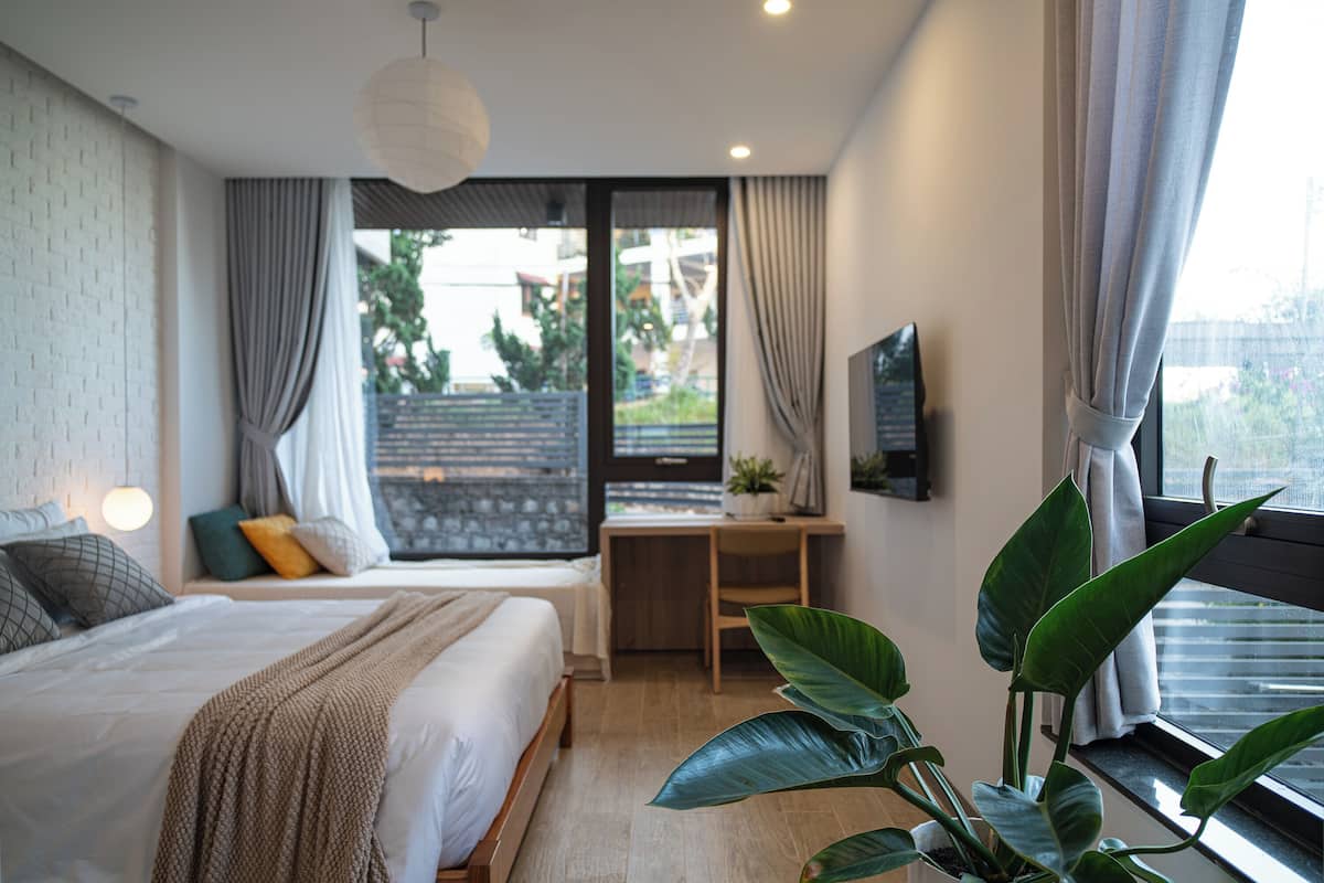 Un dormitorio moderno con cama, mesita de noche, cortinas, escritorio, silla, planta en maceta y televisor.
