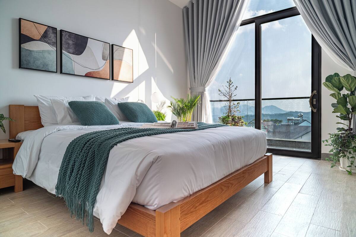 Un dormitorio moderno con una cama grande, vistas a la ciudad y un balcón con plantas.