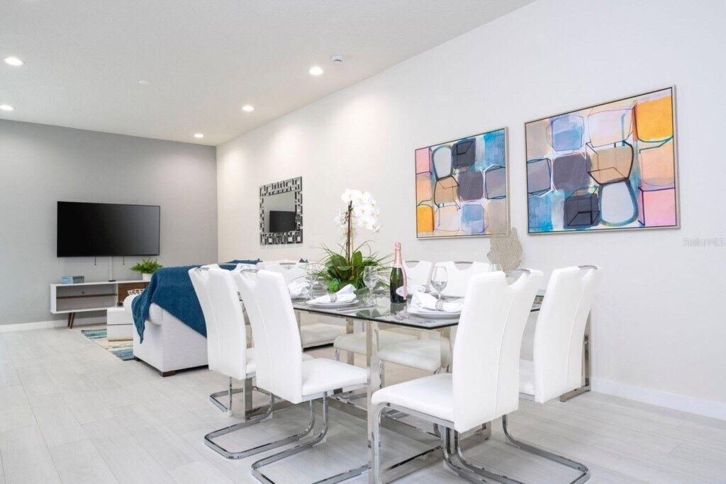A modern living room with a flat-screen TV, a sofa, a dining table with chairs, and abstract art on the walls.