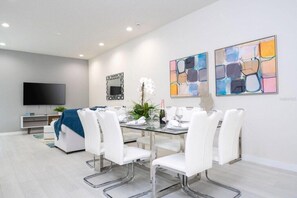 A modern living room with a flat-screen TV, a sofa, a dining table with chairs, and abstract art on the walls. - SR7512SC - Sunny Villa Near Disney (Kissimmee)