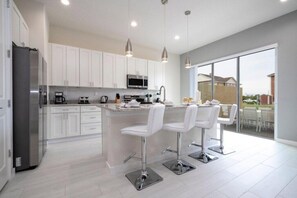 A modern kitchen with white cabinets, stainless steel appliances, and a central island with bar stools. - SR7512SC - Sunny Villa Near Disney (Kissimmee)