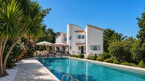 A poolside view of a white building with a curved roof, surrounded by lush greenery and a clear blue pool. -  Super Cannes villa D Aurus (Vallauris)