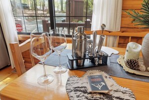 A wooden table with two wine glasses, a cocktail shaker, and a book titled 'Cocktails Recipes' on a placemat. - Pine Noir - Blue Ridge Cabin w Hot Tub, Outdoor Cinema, Dog Friendly (Blue Ridge)