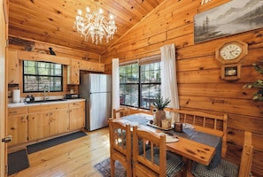 A wooden cabin with a kitchen, dining area, and a large window. - Pine Noir - Blue Ridge Cabin w Hot Tub, Outdoor Cinema, Dog Friendly (Blue Ridge)