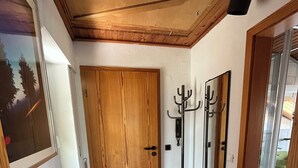 Un corridoio con una porta in legno, un appendiabiti, uno specchio e un termosifone.