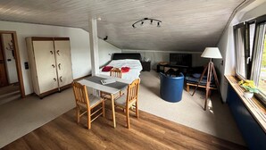 A compact room with a bed, a small table, two chairs, a desk, a lamp, and a window with a view.