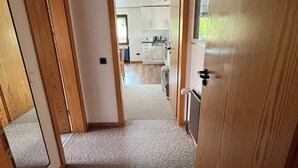A hallway leading to a kitchen with wooden flooring and a ceiling fan.
