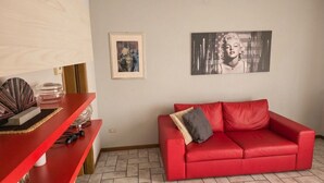 Uma sala de estar com um sofá vermelho, uma mesa de centro com objetos decorativos e duas obras de arte emolduradas na parede.