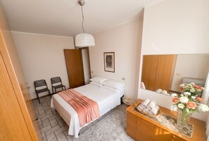 Ein Schlafzimmer mit einem Bett, zwei Stühlen, einer Kommode mit Handtüchern, einem Spiegel und einer Hängelampe.