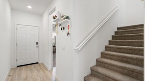 Un pasillo con una escalera alfombrada, una puerta blanca y un estante en la pared con objetos.