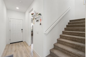 A hallway with a carpeted staircase, a white door, and a wall-mounted shelf with items.