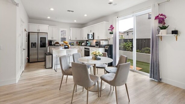 Una cocina moderna con gabinetes blancos, un refrigerador de acero inoxidable y un comedor con una mesa redonda y sillas.