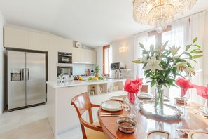 Eine moderne Küche mit Edelstahlgeräten, ein Essbereich mit Holztisch und eine Pendelleuchte.