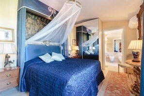 Ein Schlafzimmer mit einem großen Bett, einem Baldachin, einem Spiegel, einem Nachttisch und einem Beistelltisch.