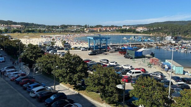 Un port de plaisance situé sur la côte, avec des voitures et des bateaux amarrés, ainsi qu’une zone de plage.