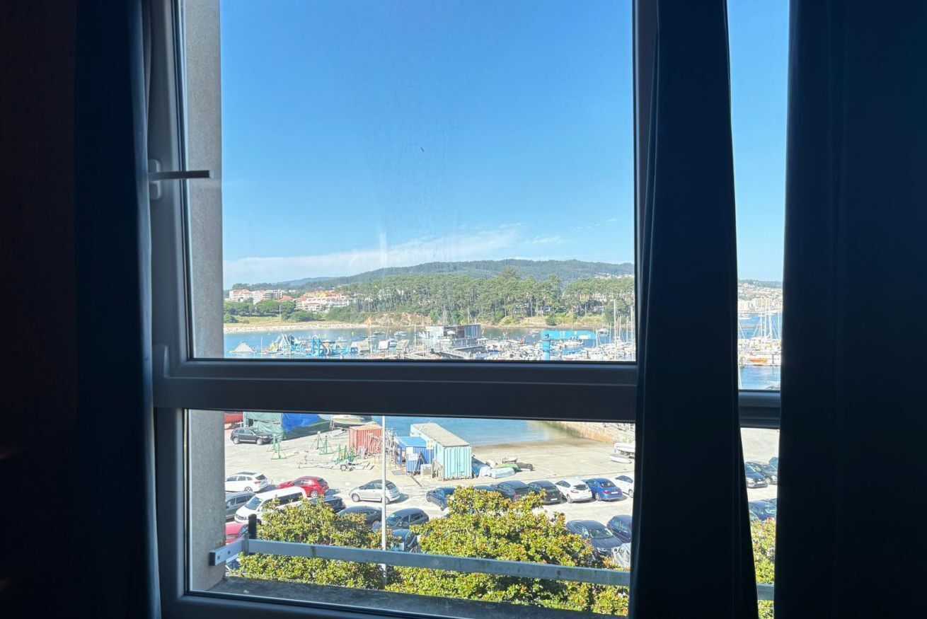 A view through a window with a clear sky, a parking lot, and a distant landscape with buildings and greenery.